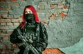 Airsoft red-hair woman in uniform with machine gun beside brick wall