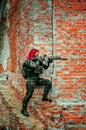 Airsoft red-hair woman in uniform with machine gun beside brick wall. Soldier aims at the sight on the ruins. Vertical photo side