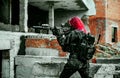 Airsoft red-hair woman in uniform with machine gun standing on knee. Soldier aims at the sight on ruine. Side view