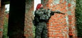 Airsoft red-hair woman in uniform with machine gun between walls. Soldier on the ruins. Horizontal photo side view