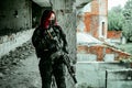 Airsoft red-head woman in uniform and put down machine gun. Soldier standing on balkony. Horizontal photo