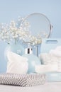 Airy blue dressing table with cosmetic accessories, mirror, basket, towel, silver bag, flowers and ceramic bowls on white wood.