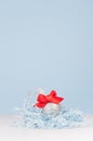 Airy soft light christmas minimalist background - silver small ball with red bow on white and pastel blue backdrop, copy space. Royalty Free Stock Photo