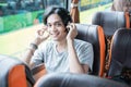 a aisan man wearing headphones smiles while listening to music while sitting by the window