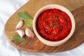 Ajvar in a bowl with garlic and spicy leaves on a wooden board. Serbian or balkan traditional food.