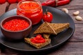 Ajvar or pindjur red vegetable spread or pepper paprika and tomato mousse in a clay bowl and glass jar in a black plate on a Royalty Free Stock Photo