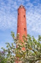 Akmensrags lighthouse on sunny spring day surrounded by blooming apple trees and lilac