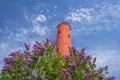 Akmensrags lighthouse on sunny spring day surrounded by blooming lilac bushes