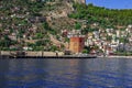 Alanya coastline with modern cottages, an ancient wall and Red Tower on the side of a mountain against a backdrop of blue water.