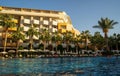 Wide angle shot of a hotel with multiple floors surrounded with palm trees next to swimming