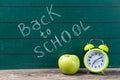 Alarm clock and apple on the green chalkboard with back to school text, education concept Royalty Free Stock Photo