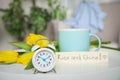 Alarm clock, aromatic morning coffee, beautiful flowers and card with RISE AND SHINE wish on white table indoors Royalty Free Stock Photo