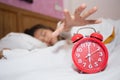 Alarm clock in bedroom with lazy woman sleeping trying to stop