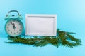 Alarm clock, blank white photo frame, cypress branches on blue background. Christmas concept Royalty Free Stock Photo