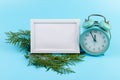 Alarm clock, blank white photo frame, cypress branches on blue background. Christmas concept Royalty Free Stock Photo