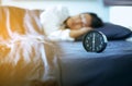 Alarm clock with blured of asian woman lethargic under blanket sleeping in bedroom in the morning