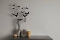 Alarm clock, burning candles and vase with paper bats  on table near white wall, space for text. Halloween decor Royalty Free Stock Photo