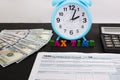 Tax form 1040, alarm clock, calculator, dollars and the word `tax time`.