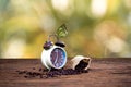 Alarm clock with coffee beans and butterfly on wooden table with morning light,