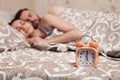 Alarm clock with couple sleeping on background. Royalty Free Stock Photo