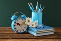 Alarm clock, flowers and set of stationery on wooden table near chalkboard. Teacher`s Day Royalty Free Stock Photo