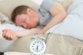 alarm clock in foreground man asleep in bed in background Royalty Free Stock Photo