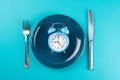 Alarm clock with fork and knife on the blue plate on blue table. Time to eat, Breakfast, Lunch Time and Dinner concept Royalty Free Stock Photo