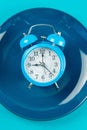 Alarm clock with fork and knife on the blue plate on blue table. Time to eat, Breakfast, Lunch Time and Dinner concept Royalty Free Stock Photo