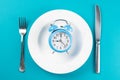 Alarm clock with fork and knife on the white plate on blue table. Time to eat, Breakfast, Lunch Time and Dinner concept Royalty Free Stock Photo