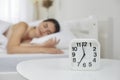 Alarm clock that is going to ring at seven in morning on background of woman sleeping in bed. Royalty Free Stock Photo