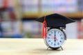 Alarm clock with graduation hat on bookshelf in the library room background, Saving money for education concept