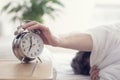 Alarm clock morning wake-up time on bedside table with man reaching to stop bell