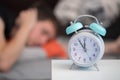 Alarm clock in the morning. Young man tries to sleep in the blurry background, insonmia