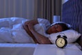 Alarm clock on nightstand near sleeping young man