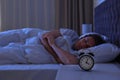 Alarm clock on nightstand near sleeping young man