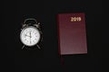 Alarm clock and notebook on black background, 2019 Royalty Free Stock Photo