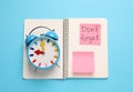 Alarm clock, notebook and reminder note with phrase Don`t forget on light blue background, top view