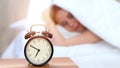 Alarm clock opposite of sleepy young woman. Early wake up, not getting enough sleep concept