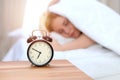 Alarm clock opposite of sleepy young woman. Early wake up, not getting enough sleep concept