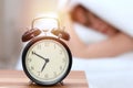 Alarm clock opposite of sleepy young woman. Early wake up, not getting enough sleep concept