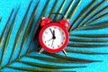 Alarm clock and palm leaf on blue bright background. Royalty Free Stock Photo