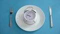 Alarm clock on plate, adhere to diet time, proper nutrition, discipline, closeup