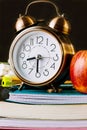 Alarm clock and red apple on top of a stack of workbooks, notebooks, pads. Pencils, pens, eraser on desktop. Black chalkboard Royalty Free Stock Photo