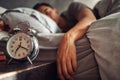 Alarm clock, relax and man sleeping in the bed of his modern apartment in the morning. Lazy, resting and closeup of a Royalty Free Stock Photo
