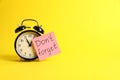 Alarm clock and reminder note with phrase Don`t forget on yellow background, space for text Royalty Free Stock Photo