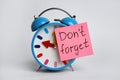 Alarm clock and reminder note with text Don`t forget on light grey background