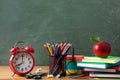 Alarm clock, school supplies and fresh red apple against blackboard background. Back to school or education concept