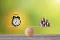 Alarm clock on seesaw balancing with stacking coins money on wooden table, meaning of business investment and saving growth with Royalty Free Stock Photo