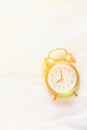 Alarm Clock Showing Eight O`Clock Lying on White Bed Blanket in Bedroom. Bright Golden Morning Sunlight Streaming Through Window
