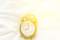 Alarm clock showing eight o`clock a.m. lying on white bed blanket in bedroom in bright golden morning sunlight streaming